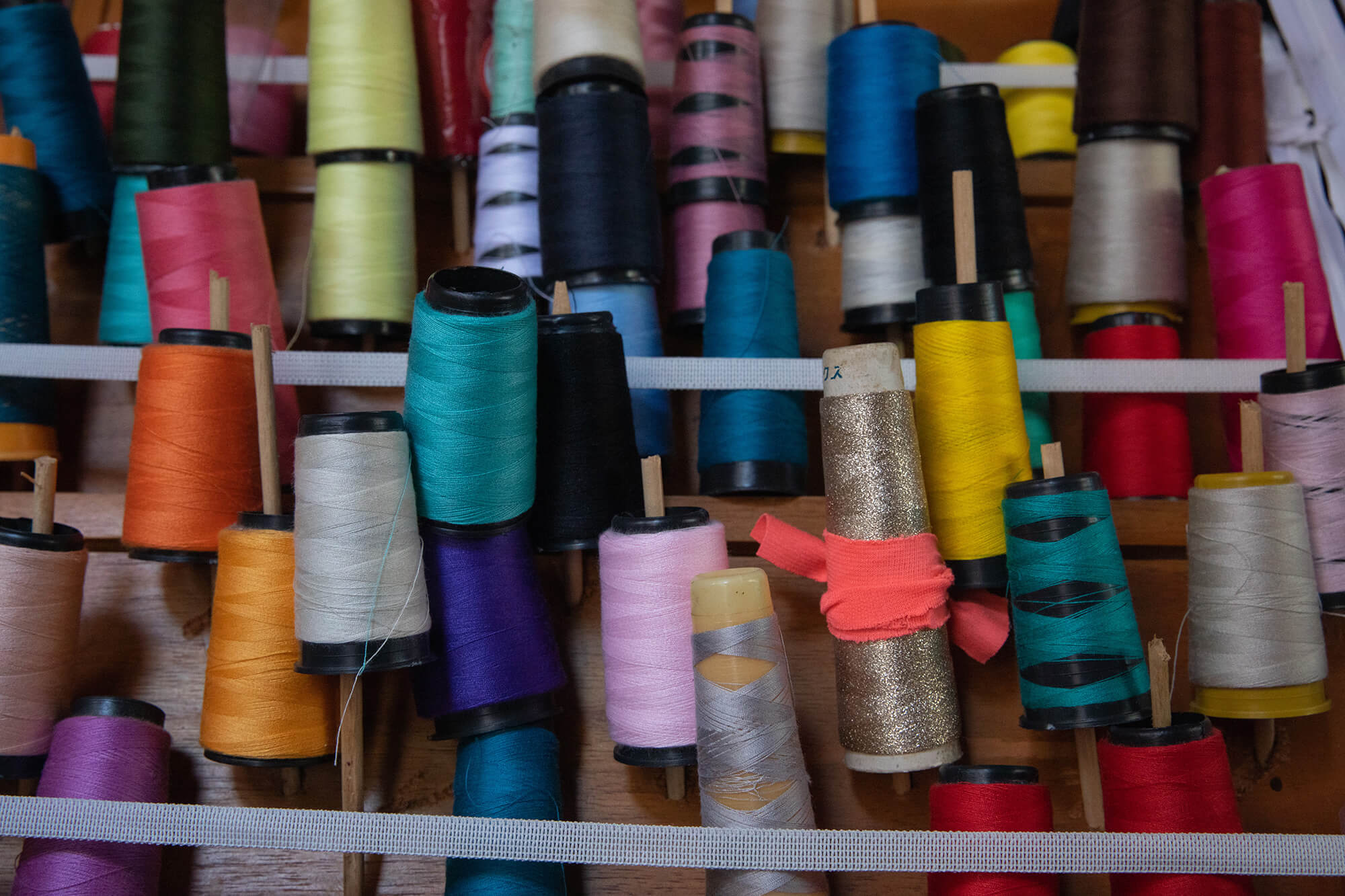 Spools of thread in many different colors sit upright on a wooden shelf in Alava’s workshop. These threads are used for sewing various items.