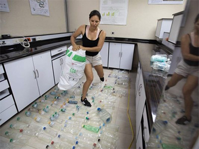 Daniela maneuvers around rows of plastic bottles laid out on the floor carrying a bag with more plastics at her side.